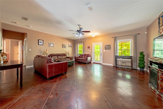 living room with a wealth of natural light, a ceiling fan, visible vents, and dark tile patterned flooring