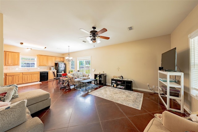 living area featuring ceiling fan with notable chandelier, dark tile patterned floors, visible vents, and a healthy amount of sunlight