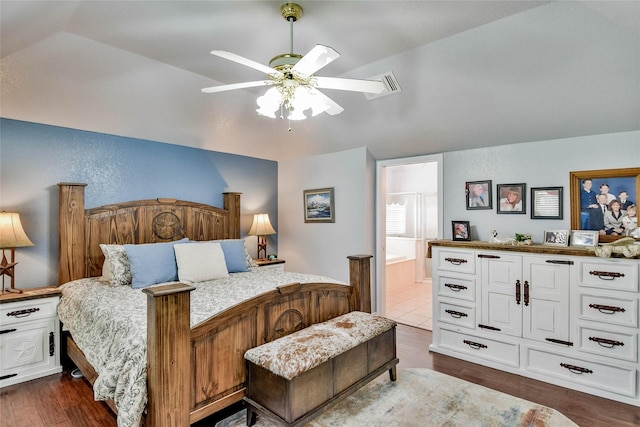 bedroom with ceiling fan, vaulted ceiling, dark wood-type flooring, and ensuite bathroom