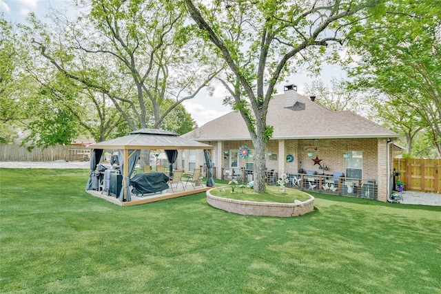 rear view of house featuring a gazebo, a chimney, fence, brick siding, and a lawn