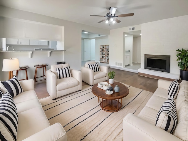 living area featuring a fireplace, wood finished floors, visible vents, and ceiling fan