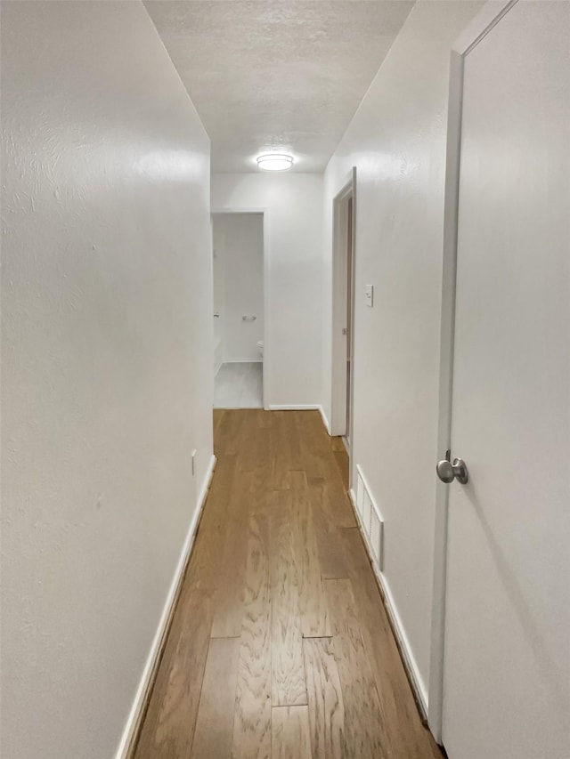 hallway featuring light wood-type flooring, baseboards, and visible vents