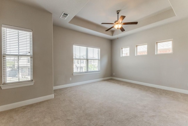 empty room with carpet flooring, baseboards, visible vents, a ceiling fan, and a raised ceiling
