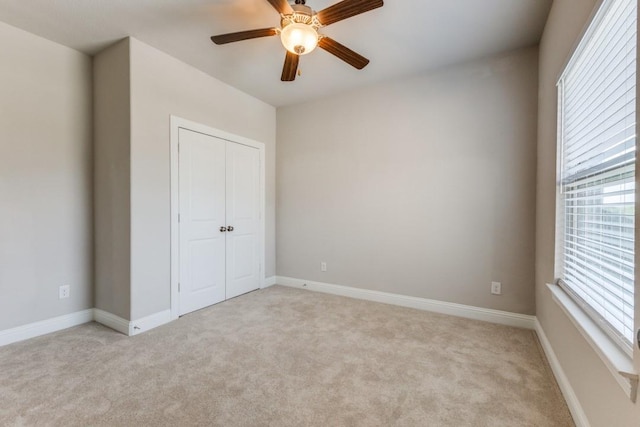 unfurnished bedroom featuring light carpet, a ceiling fan, multiple windows, and a closet