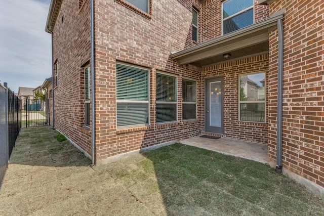 entrance to property with fence, a patio area, brick siding, and a yard