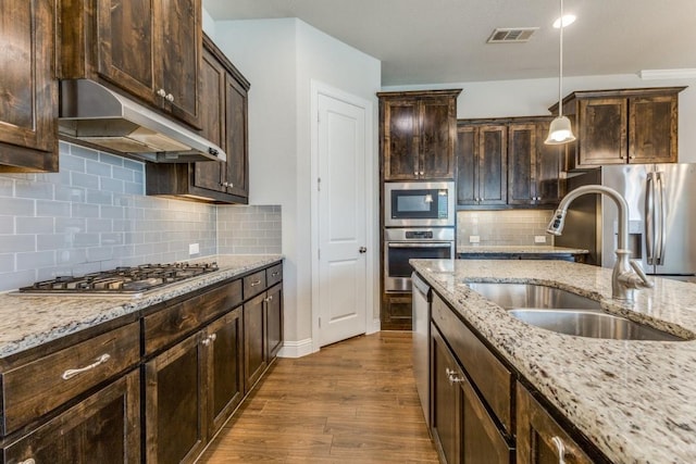 kitchen featuring a sink, dark brown cabinets, under cabinet range hood, dark wood-type flooring, and appliances with stainless steel finishes