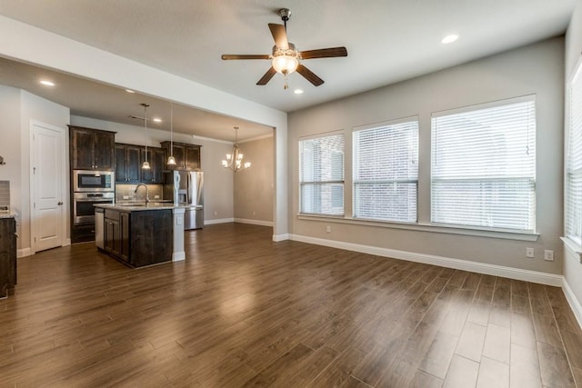 unfurnished living room with ceiling fan with notable chandelier, baseboards, recessed lighting, and dark wood-style floors