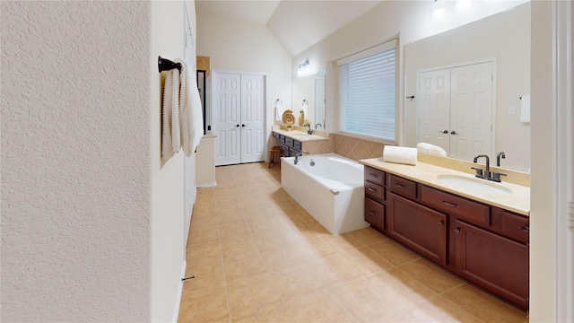 bathroom with two vanities, lofted ceiling, a garden tub, and a sink