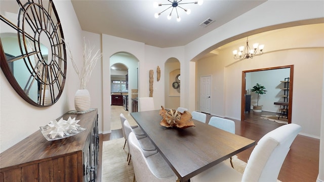 dining room featuring arched walkways, wood finished floors, visible vents, and an inviting chandelier