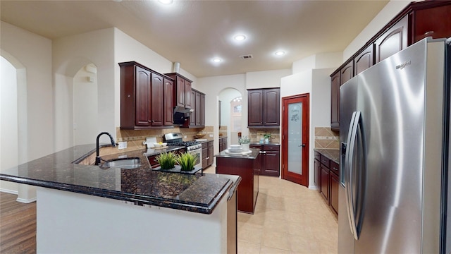 kitchen featuring a peninsula, arched walkways, a sink, visible vents, and appliances with stainless steel finishes