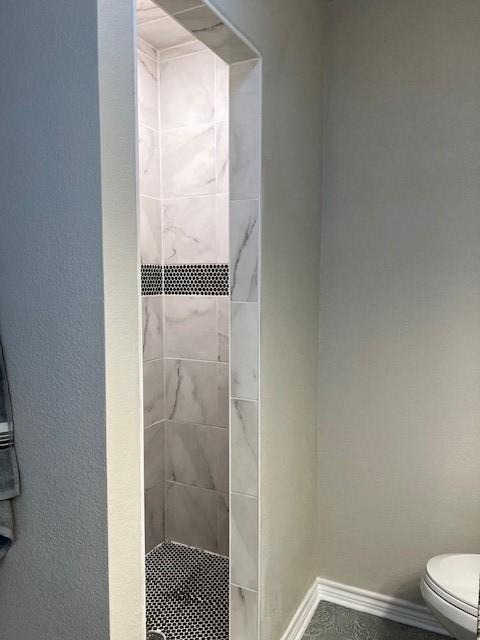 full bath with toilet, baseboards, and a tile shower