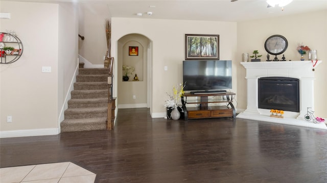 living area featuring arched walkways, a glass covered fireplace, a ceiling fan, wood finished floors, and stairway