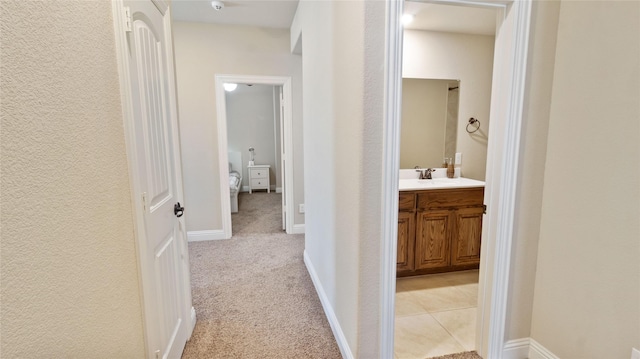 hallway with a textured wall, light carpet, and a sink
