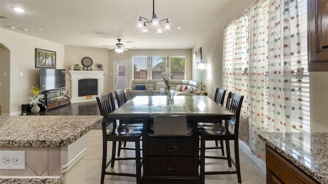 dining room with arched walkways, recessed lighting, a fireplace with raised hearth, ceiling fan with notable chandelier, and light tile patterned floors