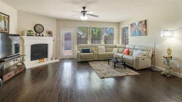 living room featuring wood-type flooring, a glass covered fireplace, a ceiling fan, and baseboards