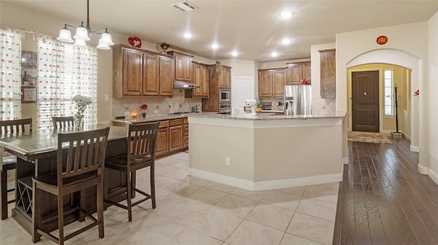 kitchen with under cabinet range hood, arched walkways, appliances with stainless steel finishes, and tasteful backsplash