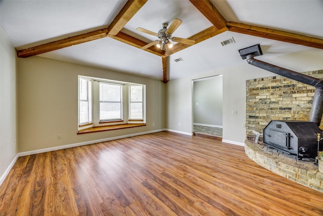 unfurnished living room featuring wood finished floors, a wood stove, visible vents, vaulted ceiling with beams, and a ceiling fan