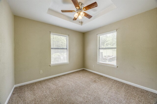 carpeted spare room with ceiling fan, baseboards, and a tray ceiling