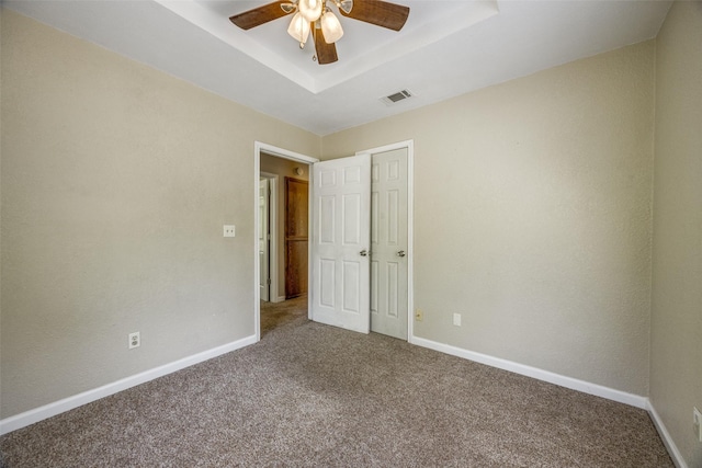 unfurnished bedroom with a tray ceiling, visible vents, carpet floors, baseboards, and ceiling fan