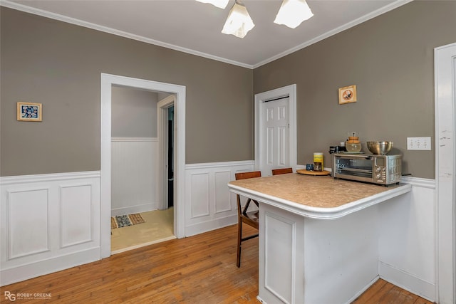 kitchen with ornamental molding, a kitchen breakfast bar, a wainscoted wall, and wood finished floors