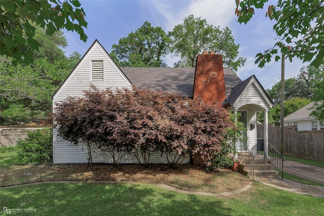 view of front of house featuring a front lawn, a shingled roof, a chimney, and fence