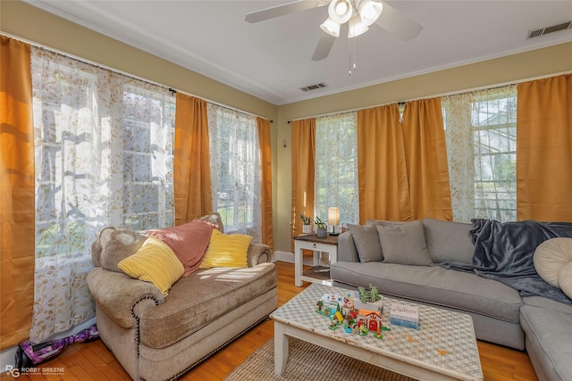 living area featuring light wood finished floors, a ceiling fan, visible vents, and ornamental molding