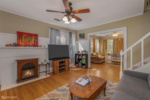 living room featuring wood finished floors, visible vents, a ceiling fan, and ornamental molding