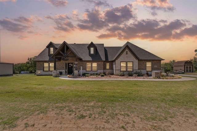 view of front of house featuring a yard, an outdoor structure, brick siding, a storage unit, and roof with shingles