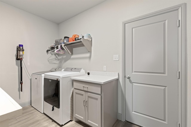 clothes washing area with light wood finished floors, baseboards, washer and clothes dryer, and cabinet space
