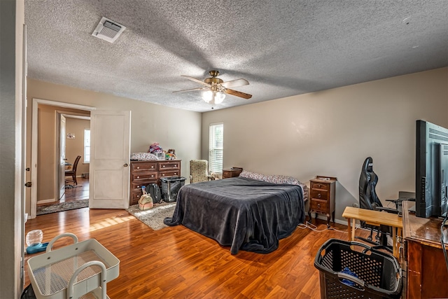 bedroom featuring wood finished floors, multiple windows, visible vents, and a textured ceiling