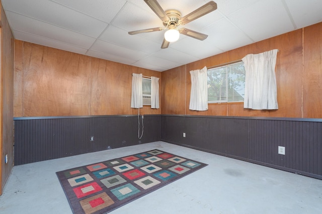 spare room with concrete floors, wood walls, a ceiling fan, and wainscoting