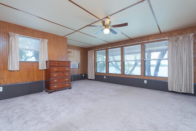 spare room featuring plenty of natural light, wooden walls, carpet flooring, and a ceiling fan