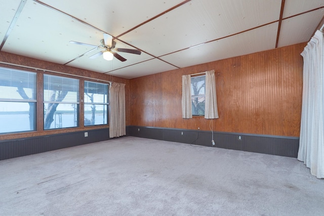 spare room featuring carpet flooring, a ceiling fan, and wood walls