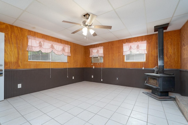 spare room featuring a paneled ceiling, cooling unit, ceiling fan, wooden walls, and a wood stove
