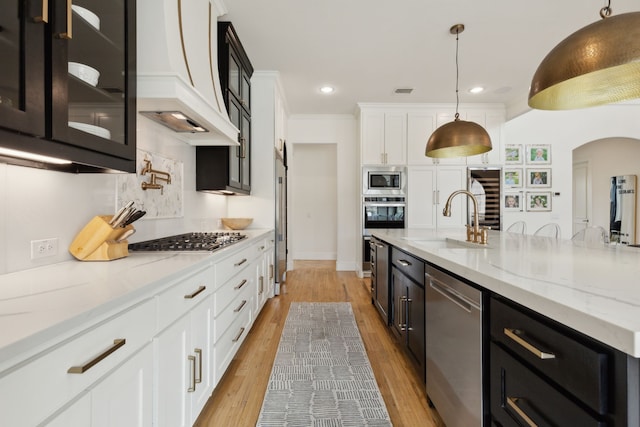 1501 Latigo Ct, Prosper, TX 75078 - kitchen featuring stainless steel appliances, a sink, custom range hood, white cabinets, and arched walkways
