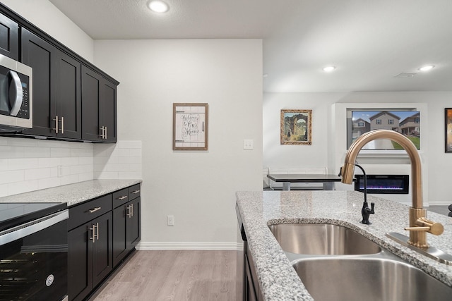 4652 Raleigh Dalton Rd, Dallas, TX 75227 - kitchen with a sink, light wood-type flooring, dark cabinetry, stainless steel microwave, and backsplash