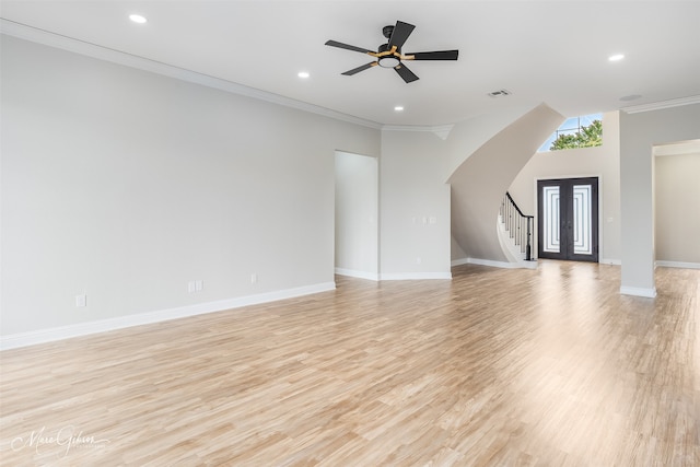 unfurnished living room with light wood finished floors, ornamental molding, arched walkways, baseboards, and stairs
