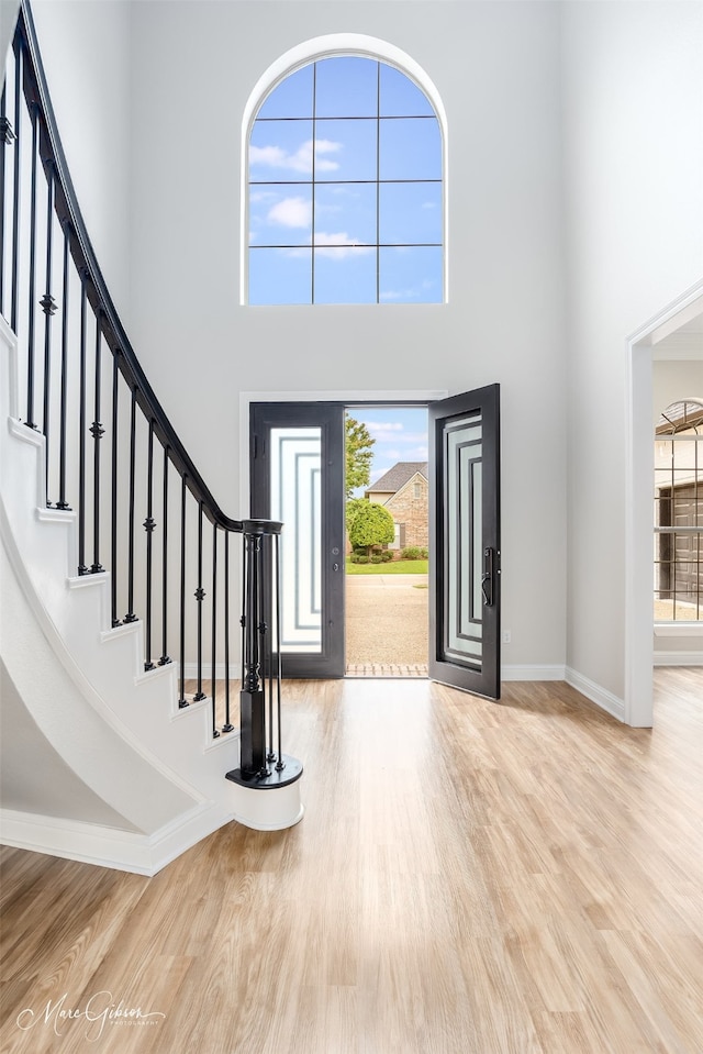foyer entrance with baseboards, wood finished floors, a towering ceiling, and stairway
