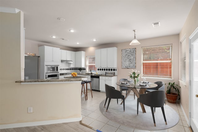 kitchen with white cabinets, stainless steel appliances, backsplash, a peninsula, and under cabinet range hood