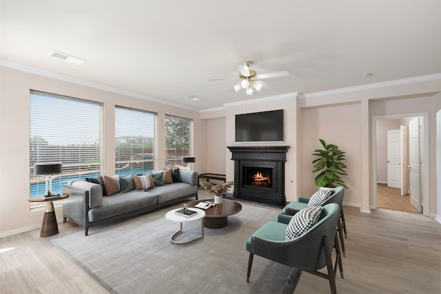 living area featuring visible vents, a ceiling fan, light wood-type flooring, crown molding, and a lit fireplace