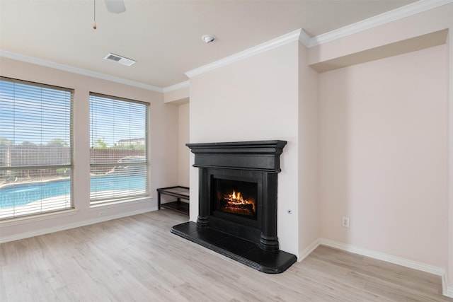 unfurnished living room with light wood-style flooring, visible vents, a lit fireplace, and crown molding