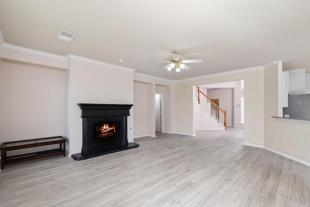unfurnished living room with visible vents, a ceiling fan, ornamental molding, light wood-style flooring, and stairs