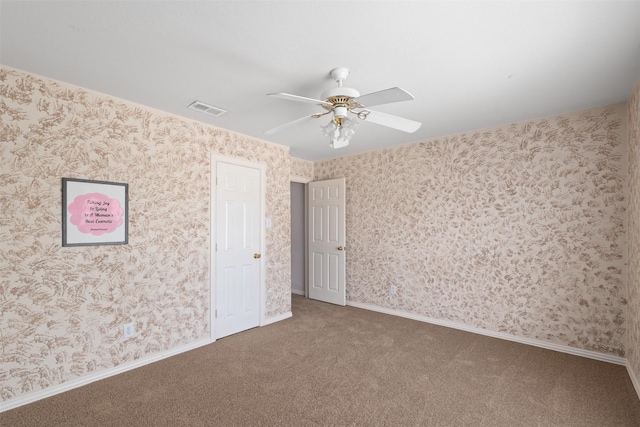carpeted empty room with wallpapered walls, visible vents, baseboards, and ceiling fan