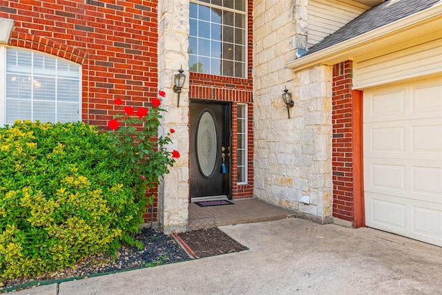 entrance to property featuring concrete driveway, brick siding, a shingled roof, and a garage