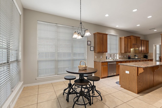 kitchen featuring stainless steel dishwasher, brown cabinets, pendant lighting, backsplash, and light stone countertops