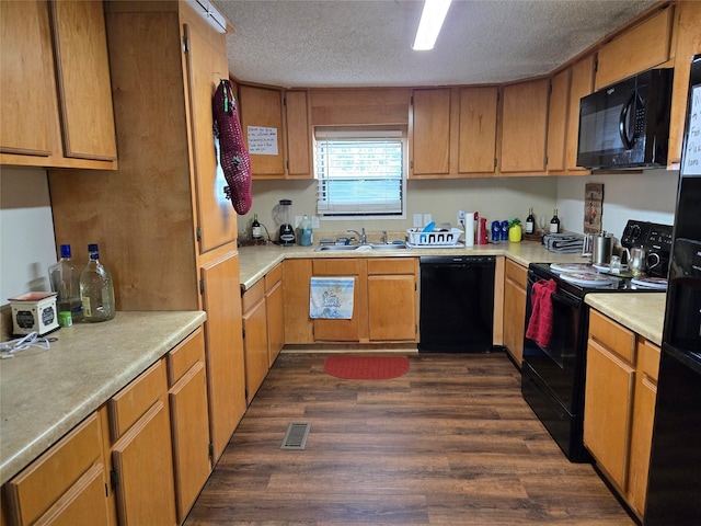 kitchen with a textured ceiling, a sink, light countertops, dark wood-type flooring, and black appliances