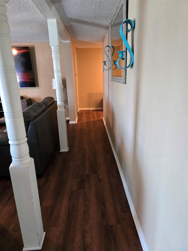 hallway featuring baseboards, wood finished floors, and a textured ceiling