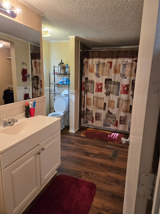 bathroom with wood finished floors, visible vents, vanity, wainscoting, and a textured ceiling