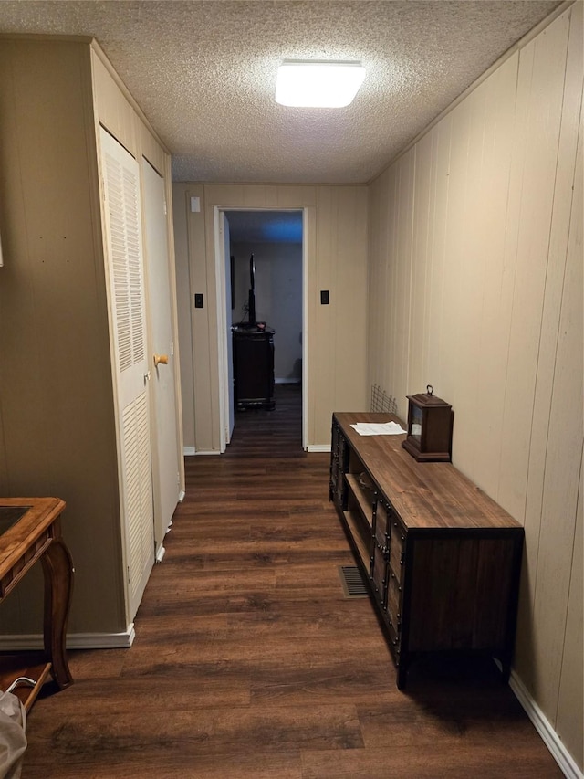 hall with visible vents, a textured ceiling, and dark wood finished floors
