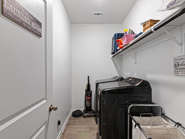 clothes washing area featuring laundry area, wood finished floors, visible vents, washing machine and clothes dryer, and baseboards